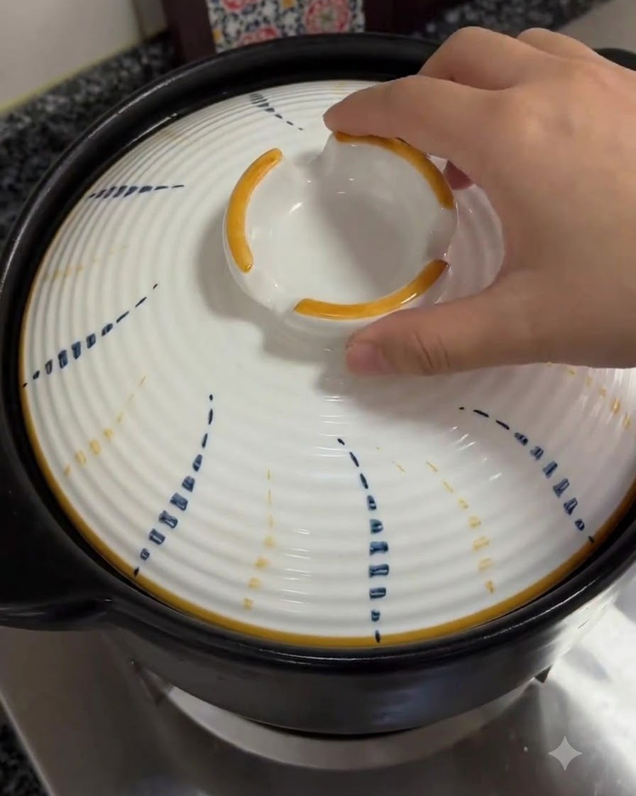A hand placing the patterned white lid back onto the simmering clay pot.