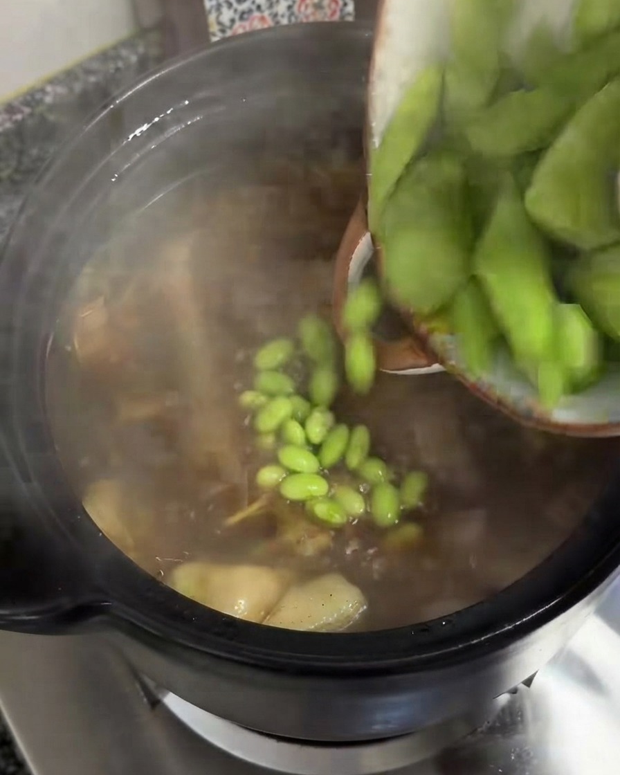 Thick slices of green celtuce being poured from a bowl into a simmering pot of soup.