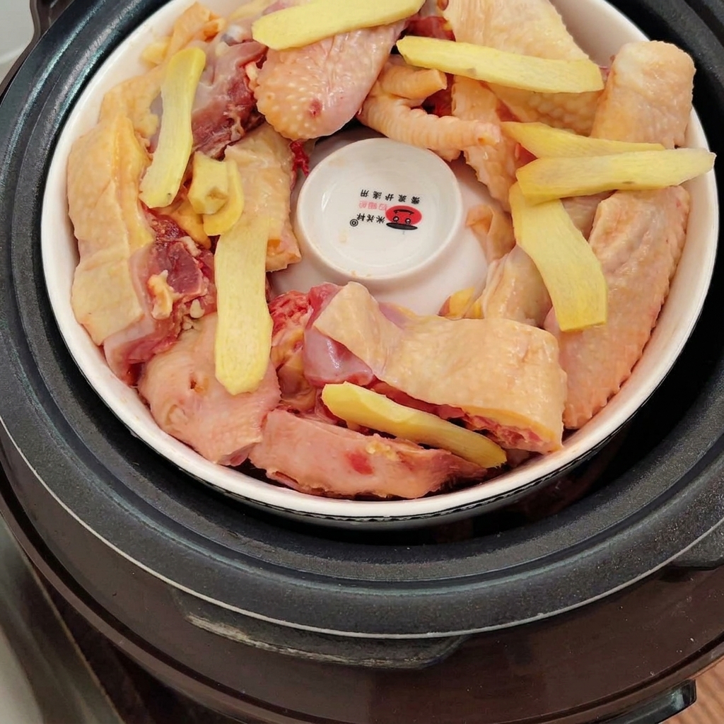 Slices of fresh ginger laid out on top of the chicken pieces inside the pot.