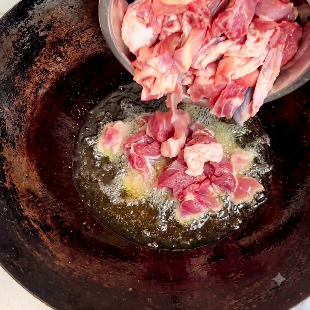 Raw chicken pieces being poured from a steel bowl into the wok containing oil and ginger.