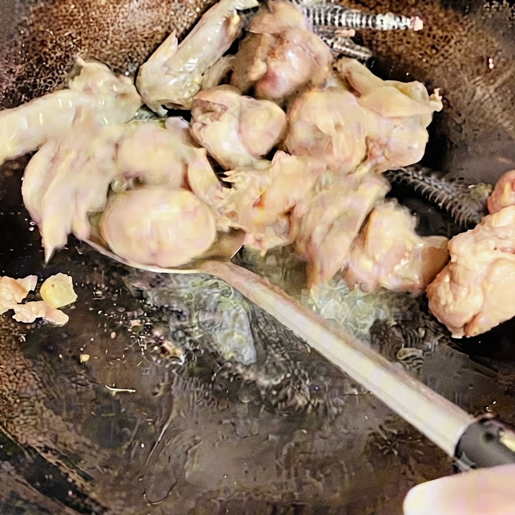 Chicken pieces being turned and stir-fried with a spatula in the wok until lightly browned.