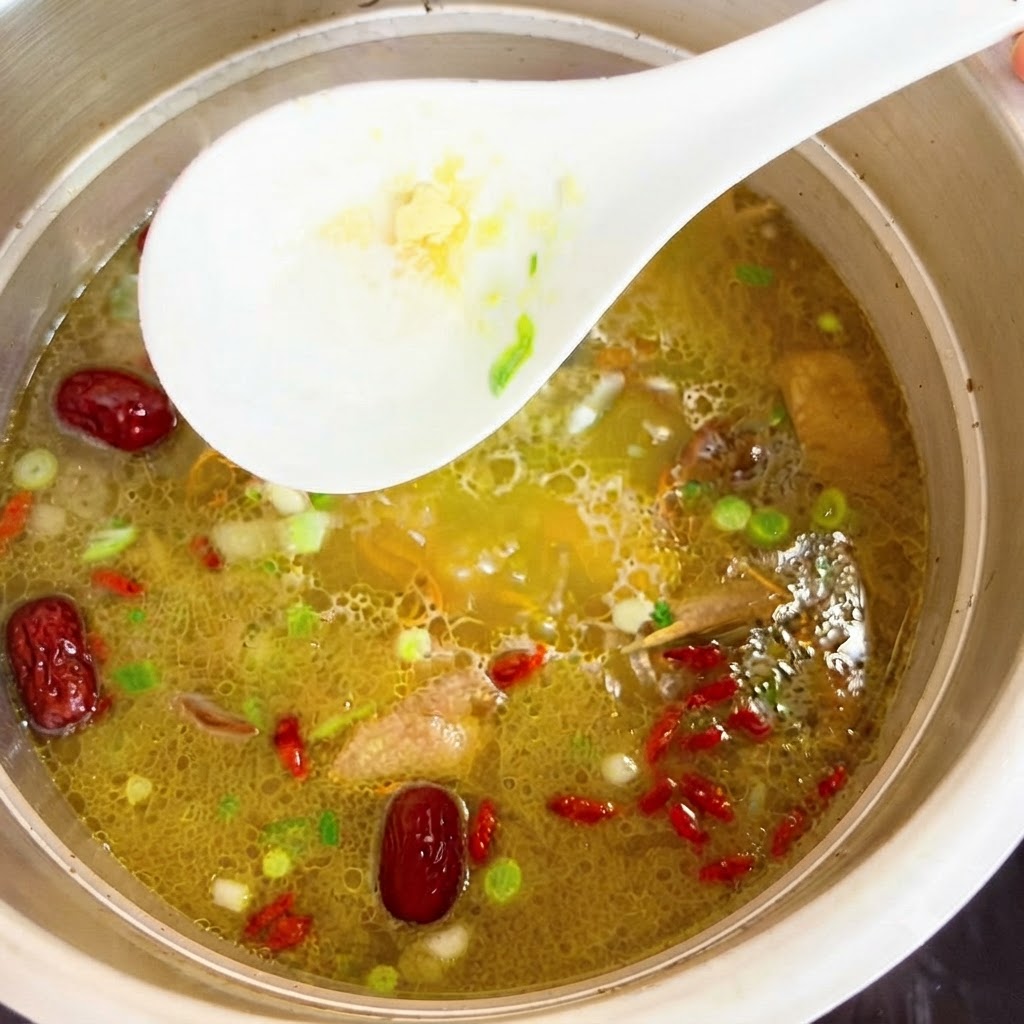 Chicken essence being stirred into the pot of hot chicken soup with a white spoon.