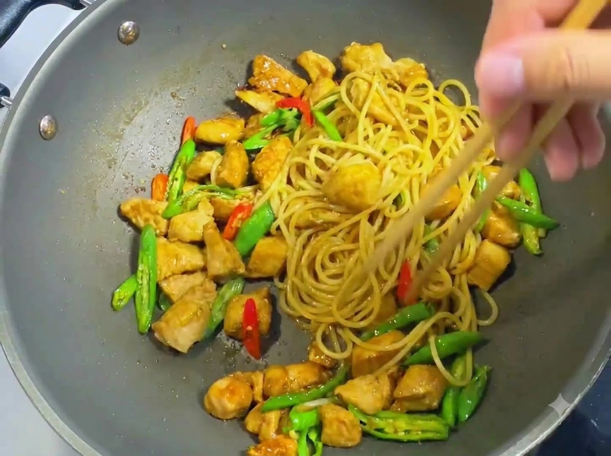 Wooden chopsticks tossing and mixing spaghetti noodles, diced chicken, sliced chilies, and dark sauce evenly in a wok.