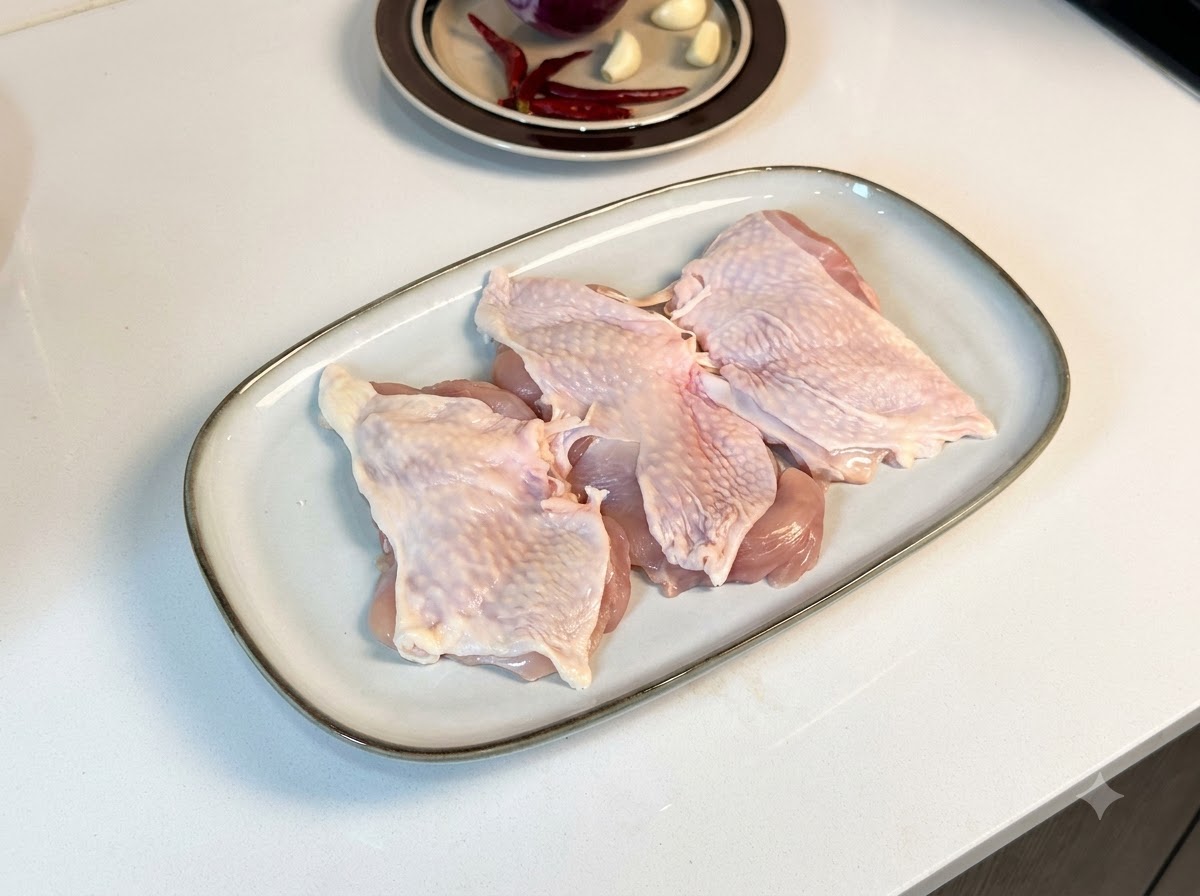 Boneless chicken thighs laid out on a white rectangular plate, coated with black pepper and seasonings.