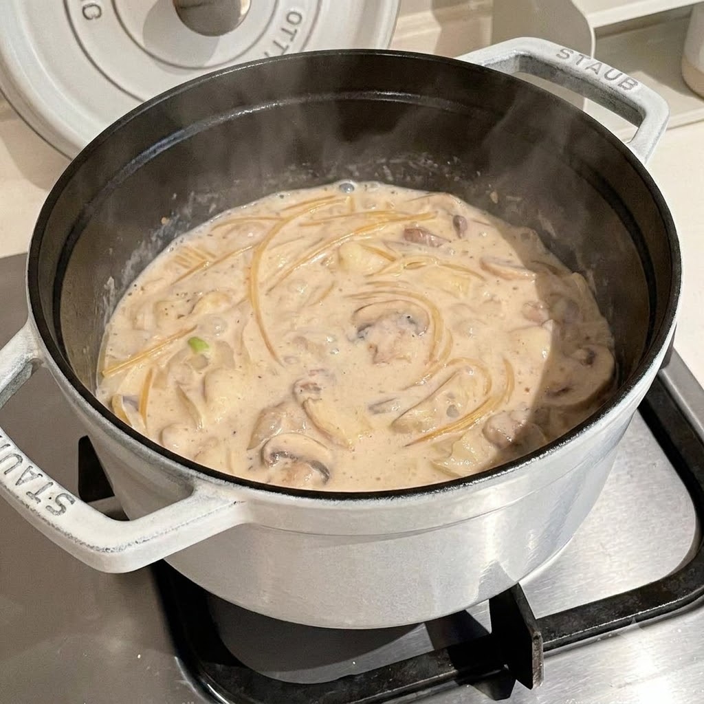 Spaghetti noodles cooking inside a simmering creamy broth inside a white pot.