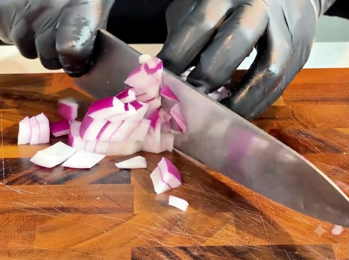 A knife chopping a raw red onion into small pieces on a wooden cutting board.