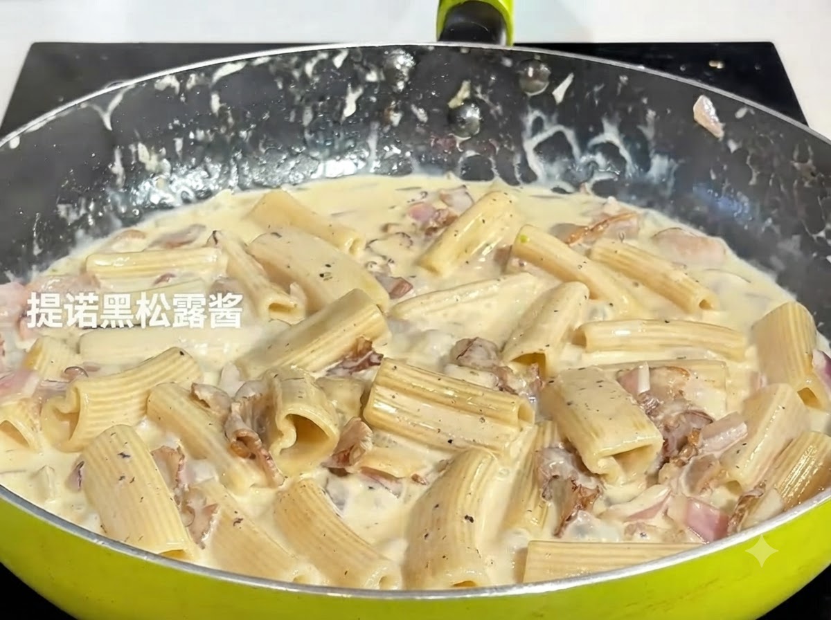 A spoonful of dark black truffle paste being added to the simmering pasta mixture in a pan.