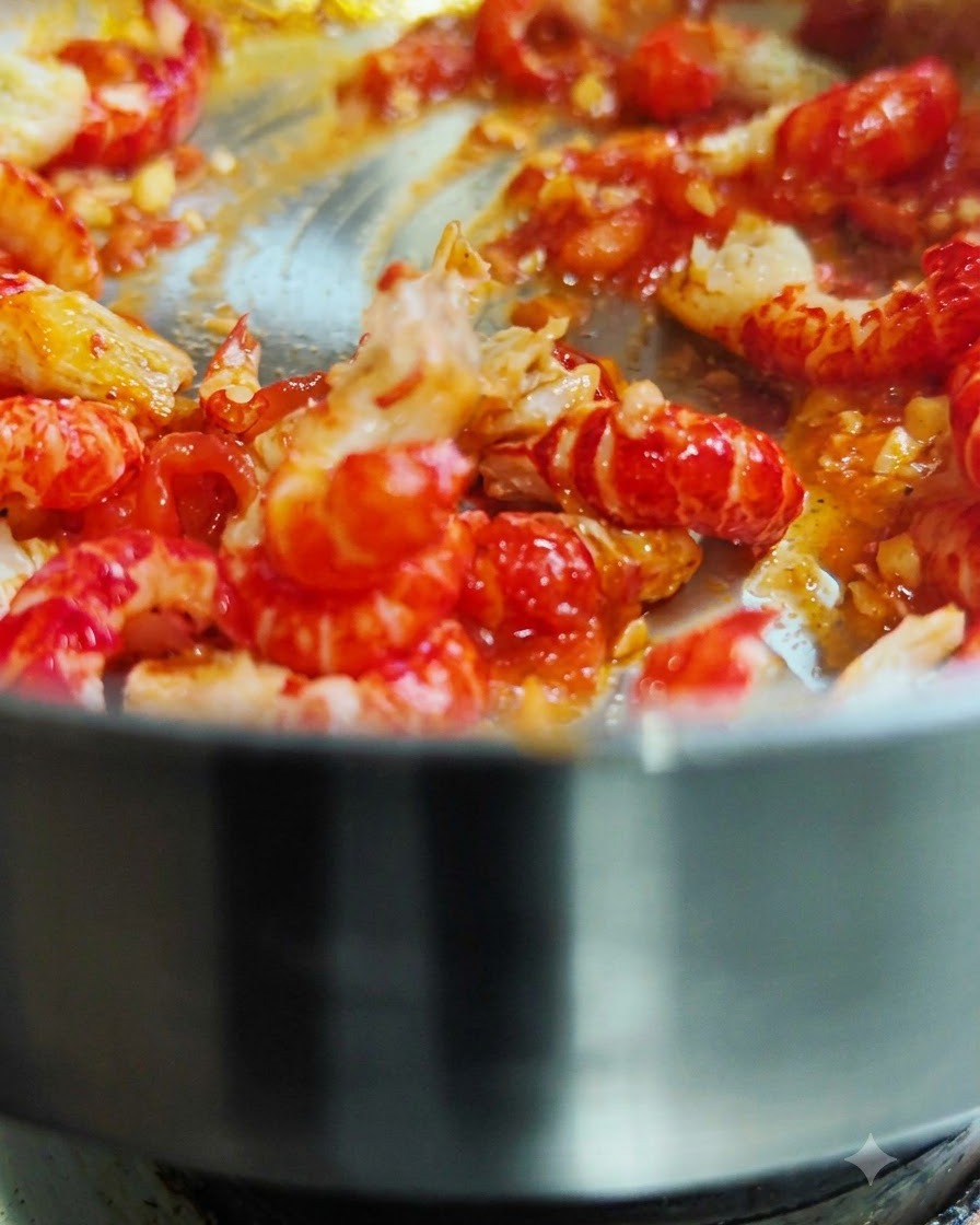Shelled crawfish tails being tossed and stir-fried in a hot pan with red tomato sauce.