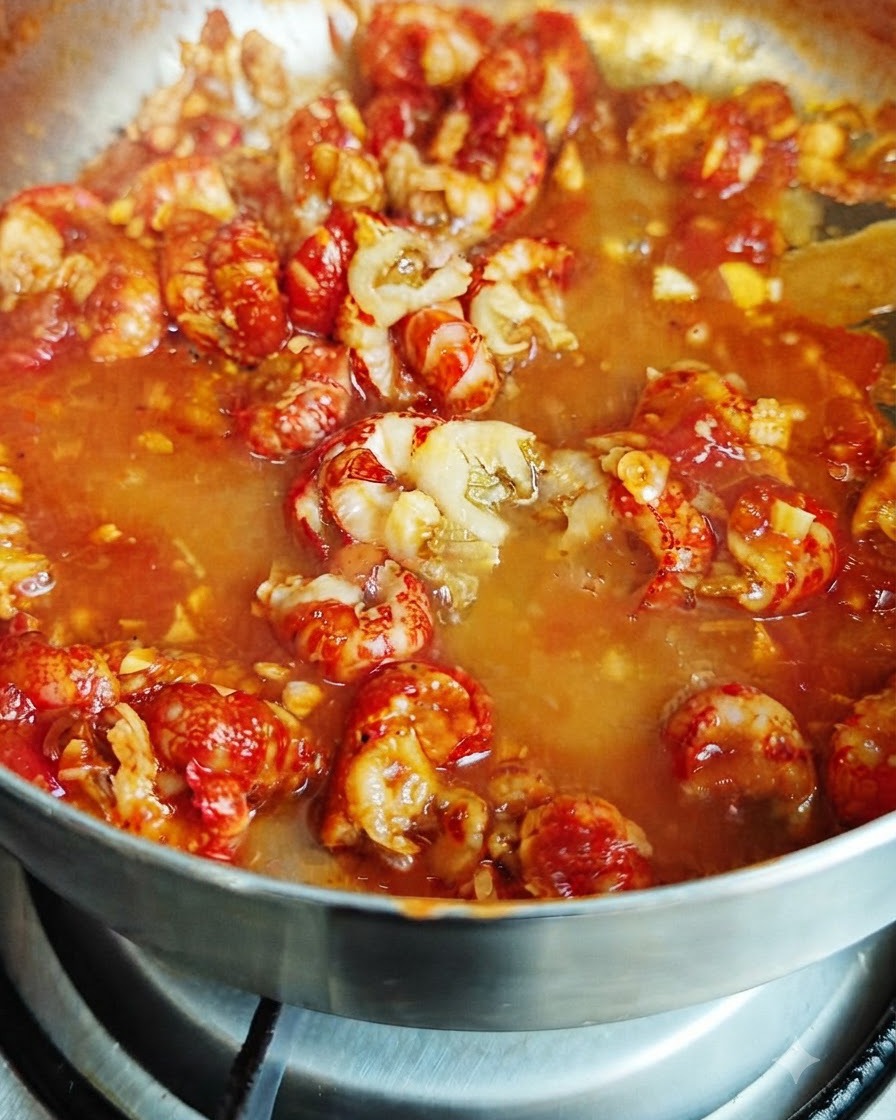 Milk being poured into the bubbling red sauce mixture containing crawfish tails.