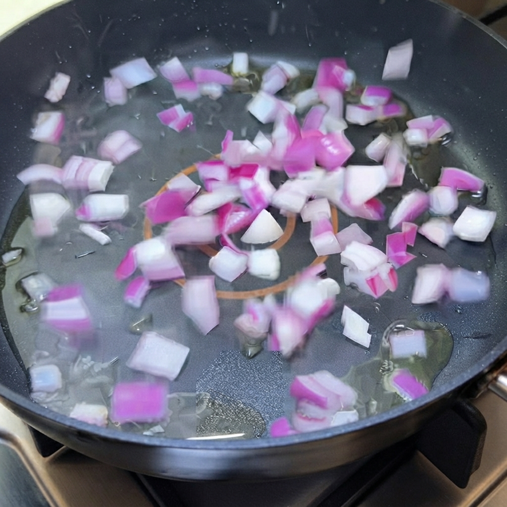 Diced red onion sizzling in oil inside a frying pan.