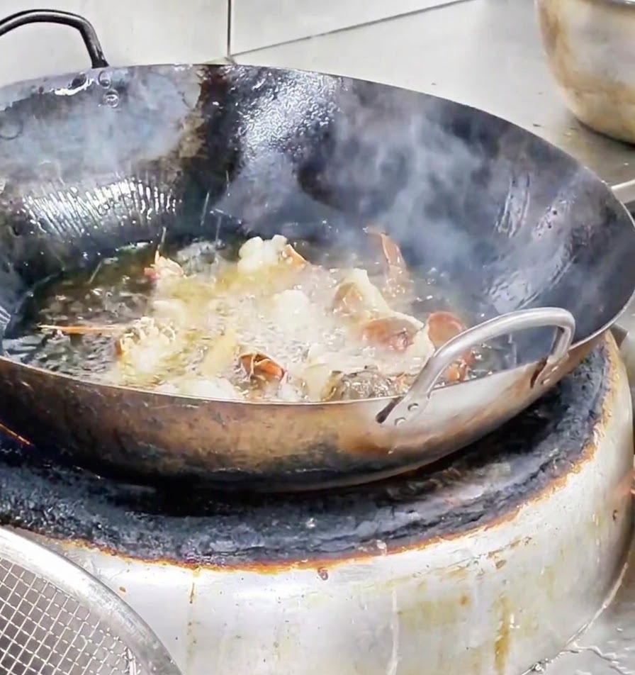 Lobster pieces frying vigorously in a wok filled with bubbling hot oil.