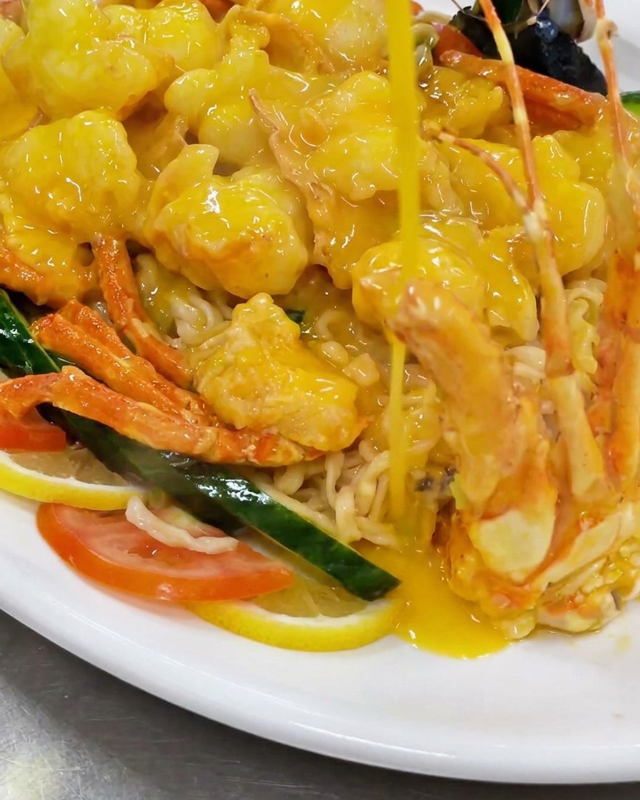 Pouring fried lobster pieces into a wok filled with a rich, bubbling yellow cheese sauce.