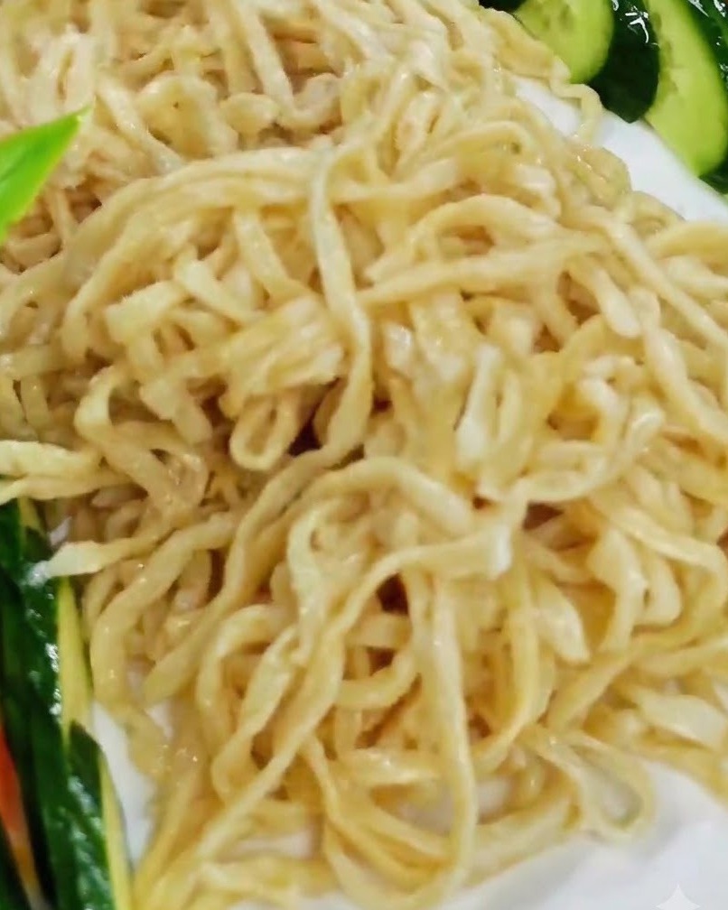 Arranging the cooked lobster pieces over the bed of noodles on a white serving plate.
