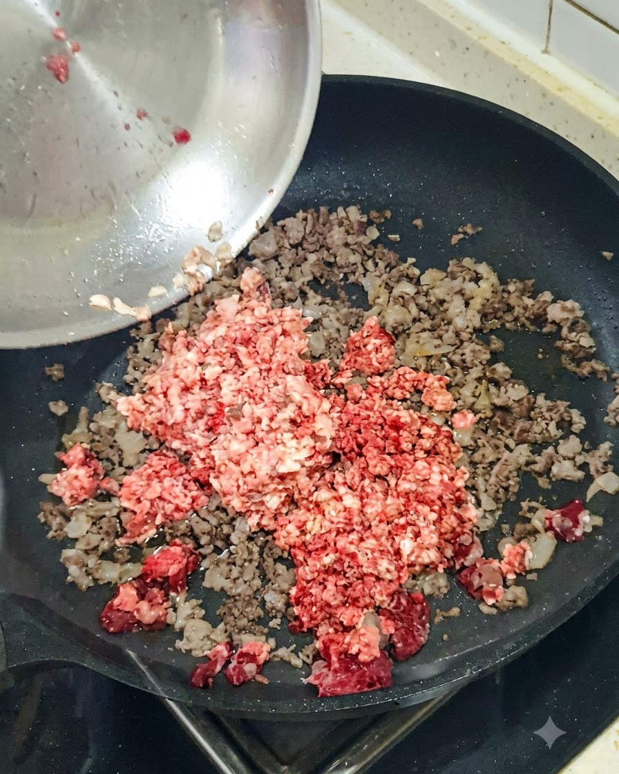 Chopped red onion being tossed into a skillet containing browned ground meat.