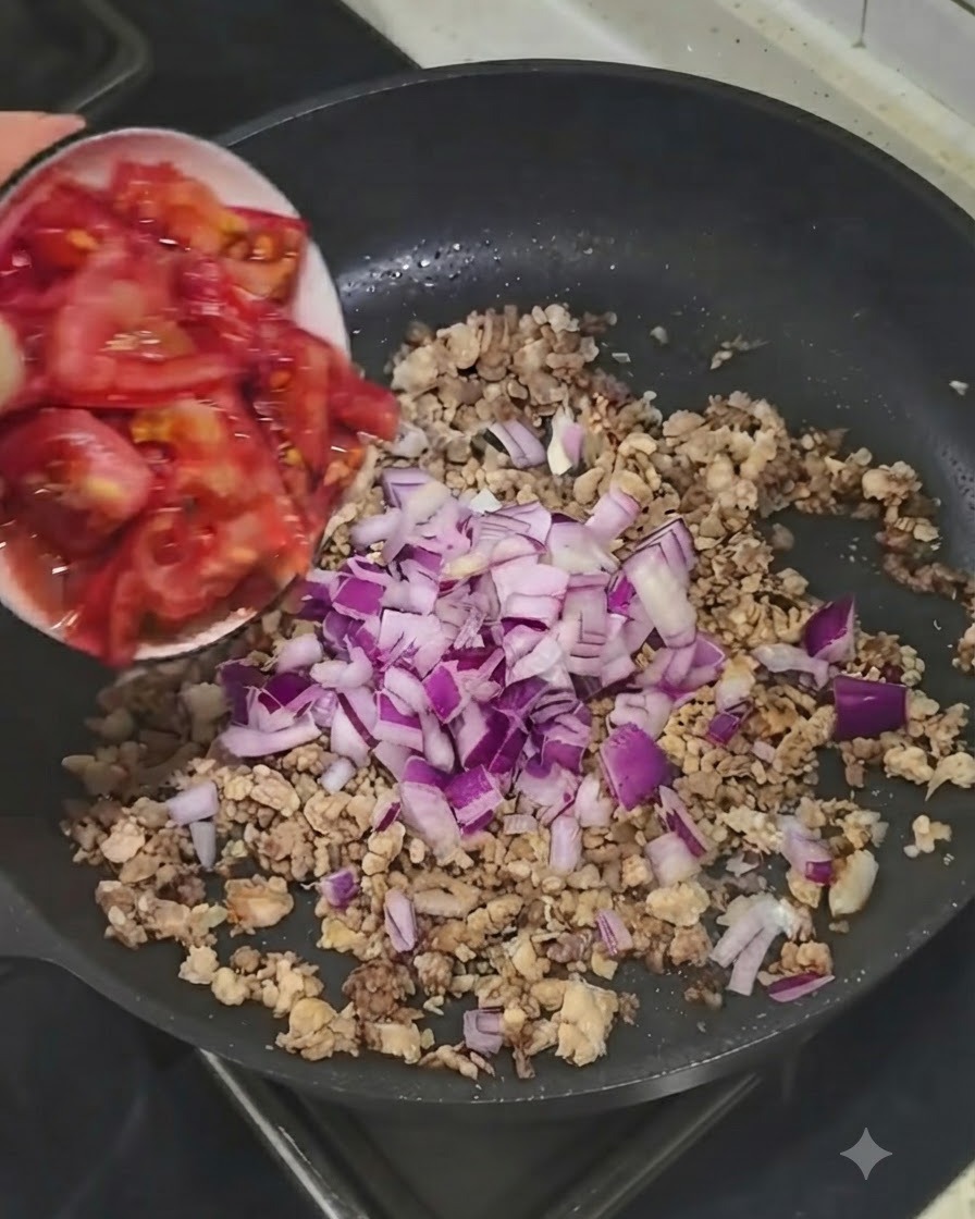 Fresh chopped tomatoes being added from a small bowl into the skillet with meat and onions.