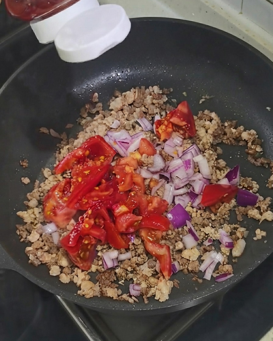 Ketchup being squeezed from a bottle directly onto the ingredients in the skillet.