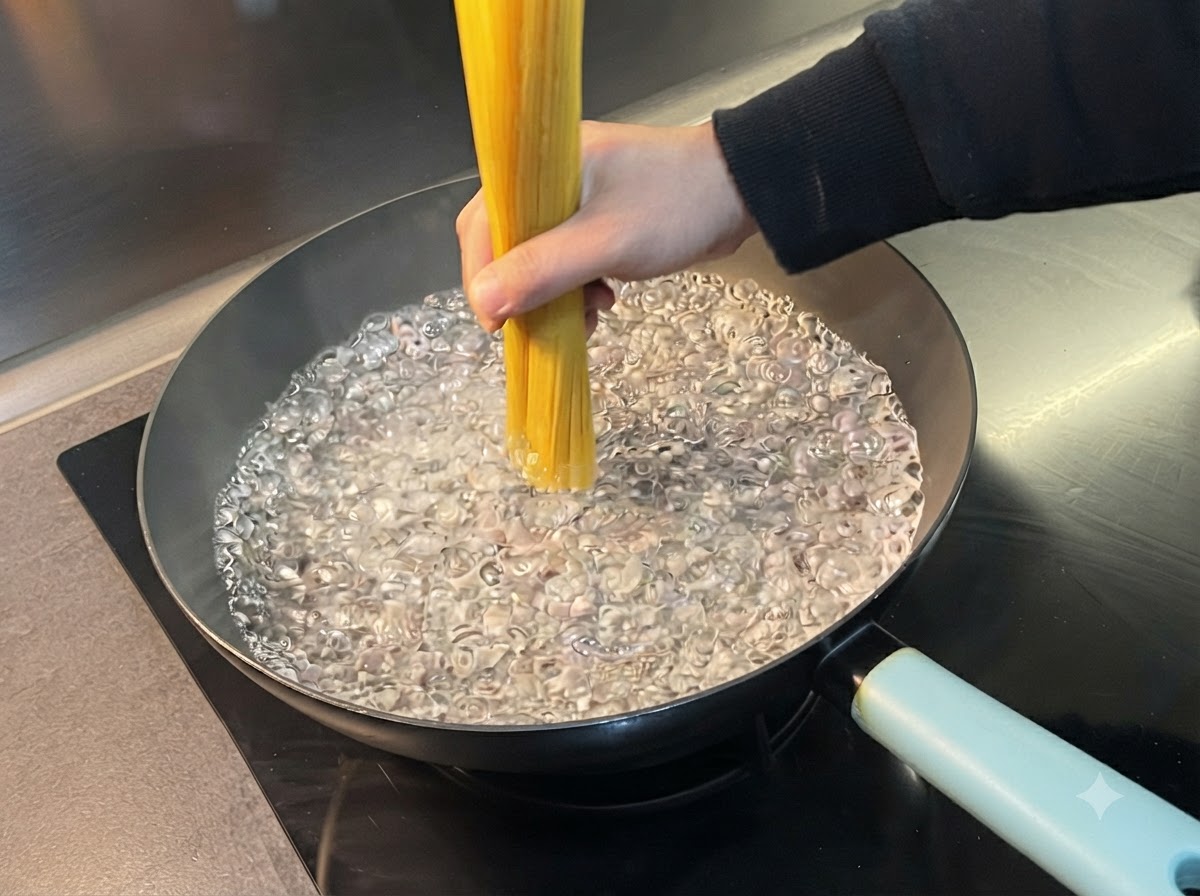 A hand vertically holding a bundle of dry spaghetti in a wide pan of vigorously boiling water.
