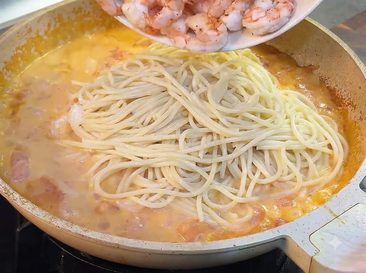 Cooked shrimp being poured from a plate into the pan with spaghetti and sauce.