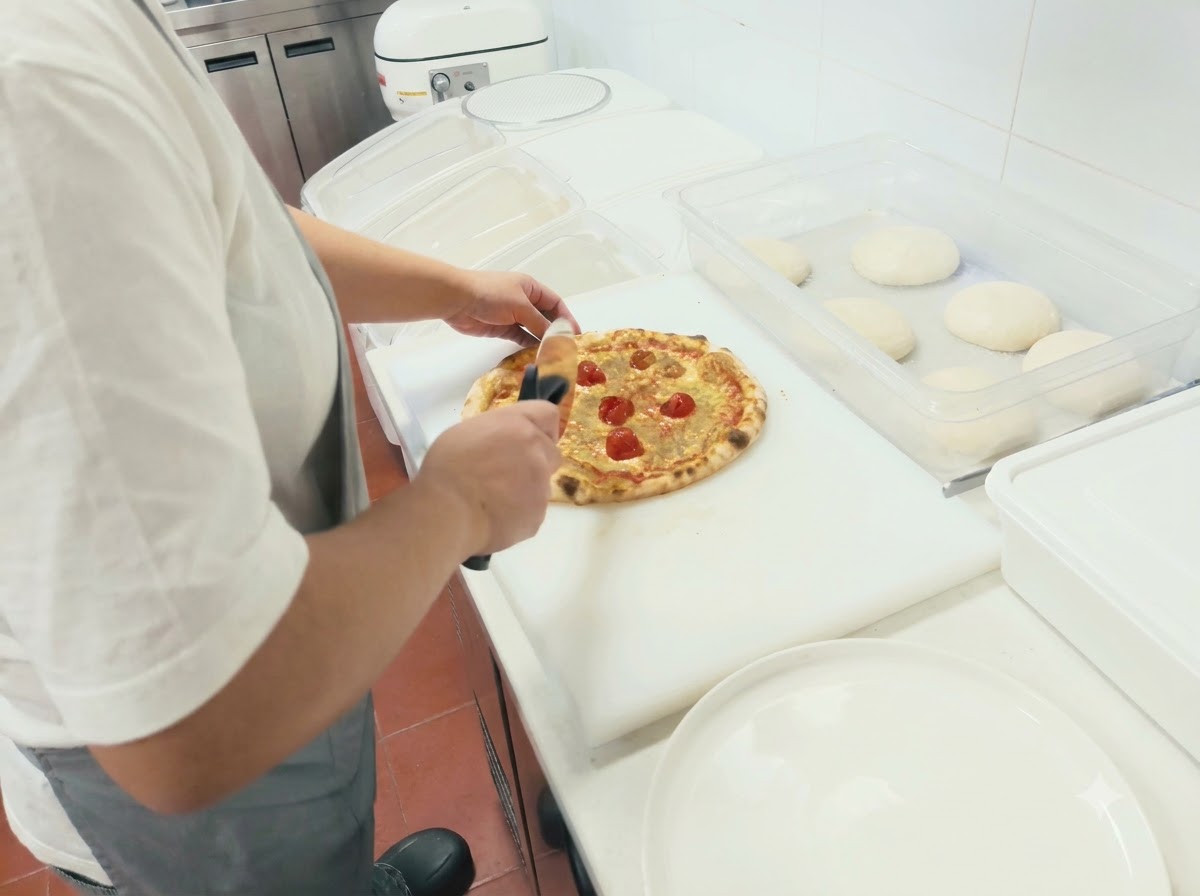 A person using a rolling pizza cutter to slice a freshly baked pizza on a white cutting board.
