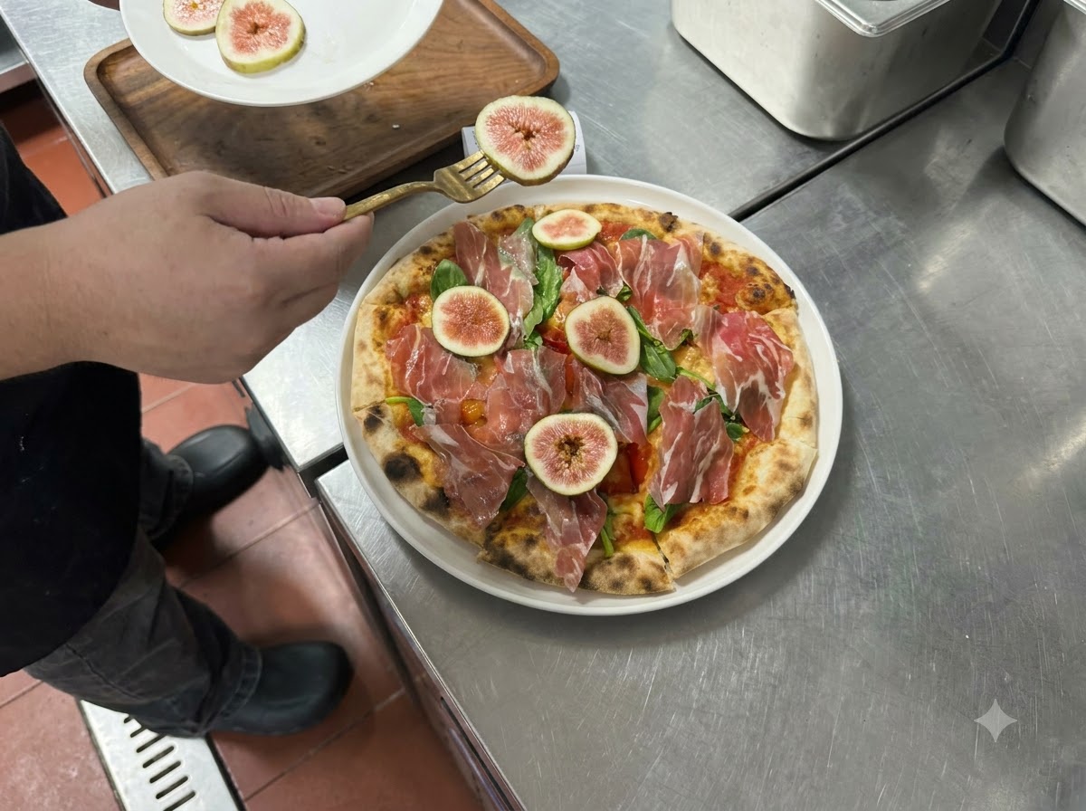 Slices of fresh figs and prosciutto being arranged on top of a cooked pizza with a fork.