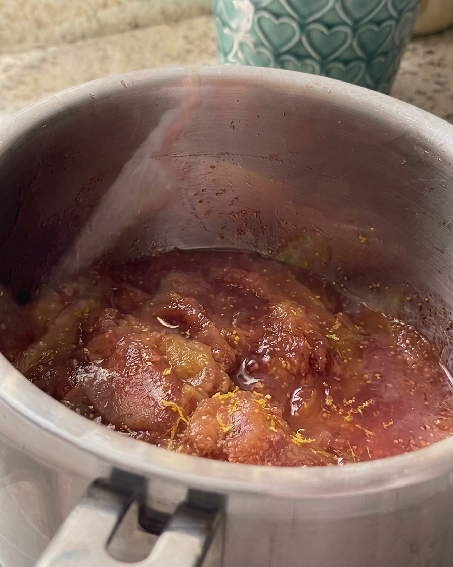 Lemon zest and juice being mixed into the simmering fig sauce in a stainless steel saucepan.