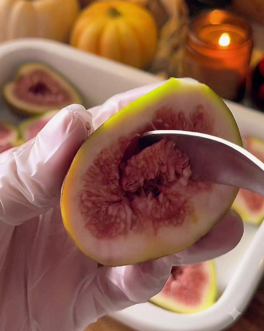 A metal spoon scooping out the center of a fig half.