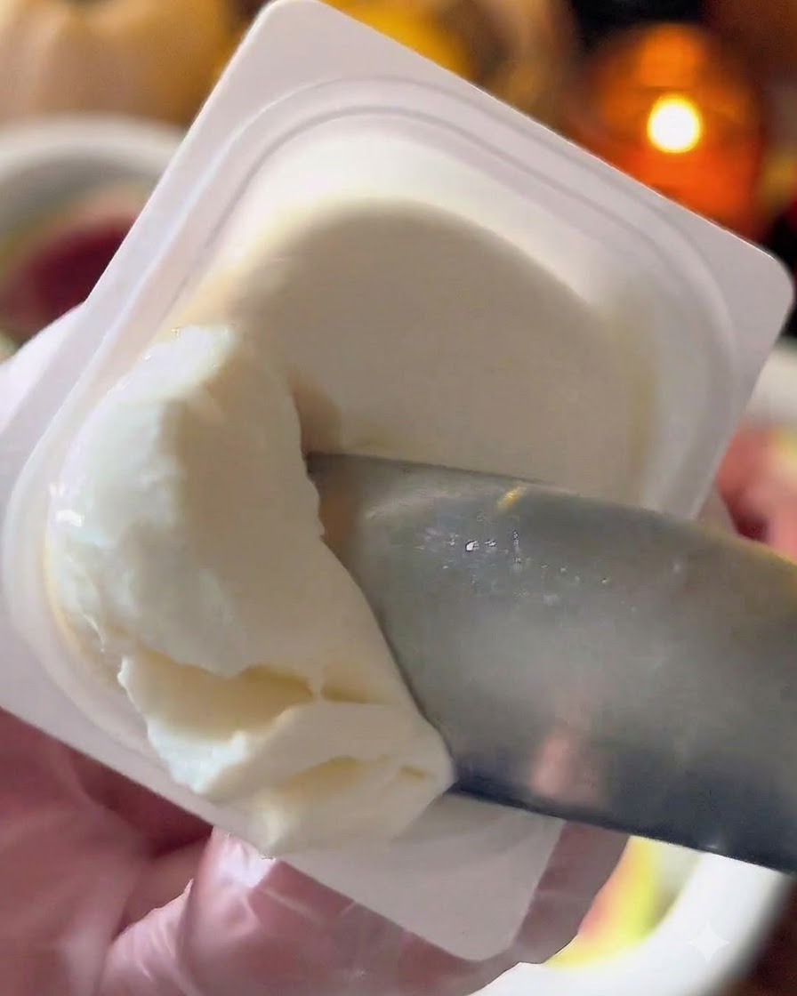 A small knife or spoon scooping white labneh cheese from a container.