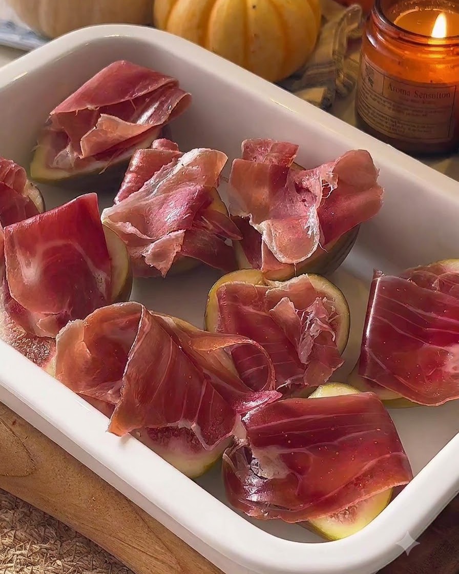 Assembled figs topped with prosciutto arranged in a white baking dish.