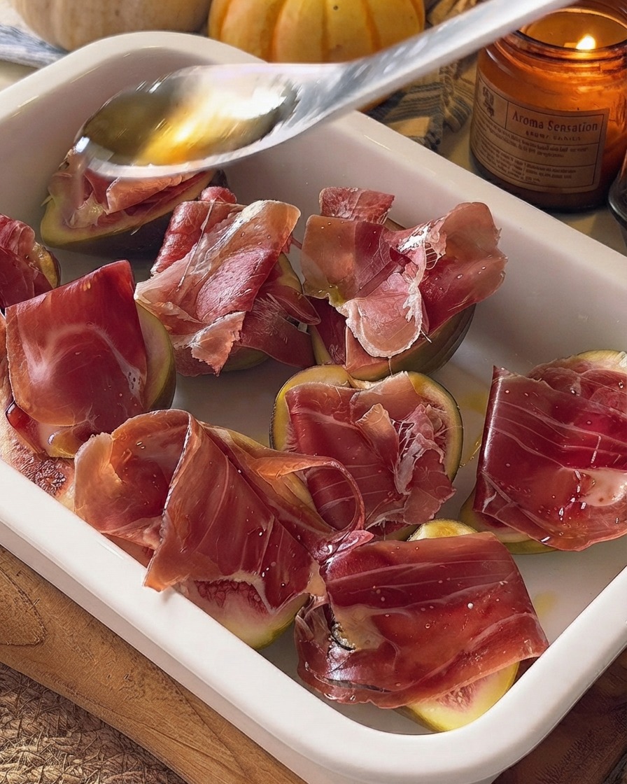 Honey being drizzled from a spoon over the prepared figs and prosciutto in a baking dish.