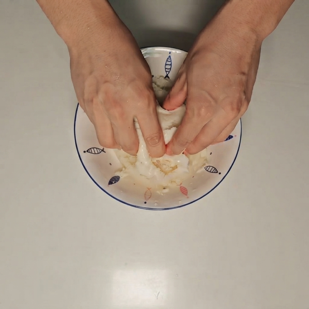 Hands crushing a wet steamed bun inside a white bowl.