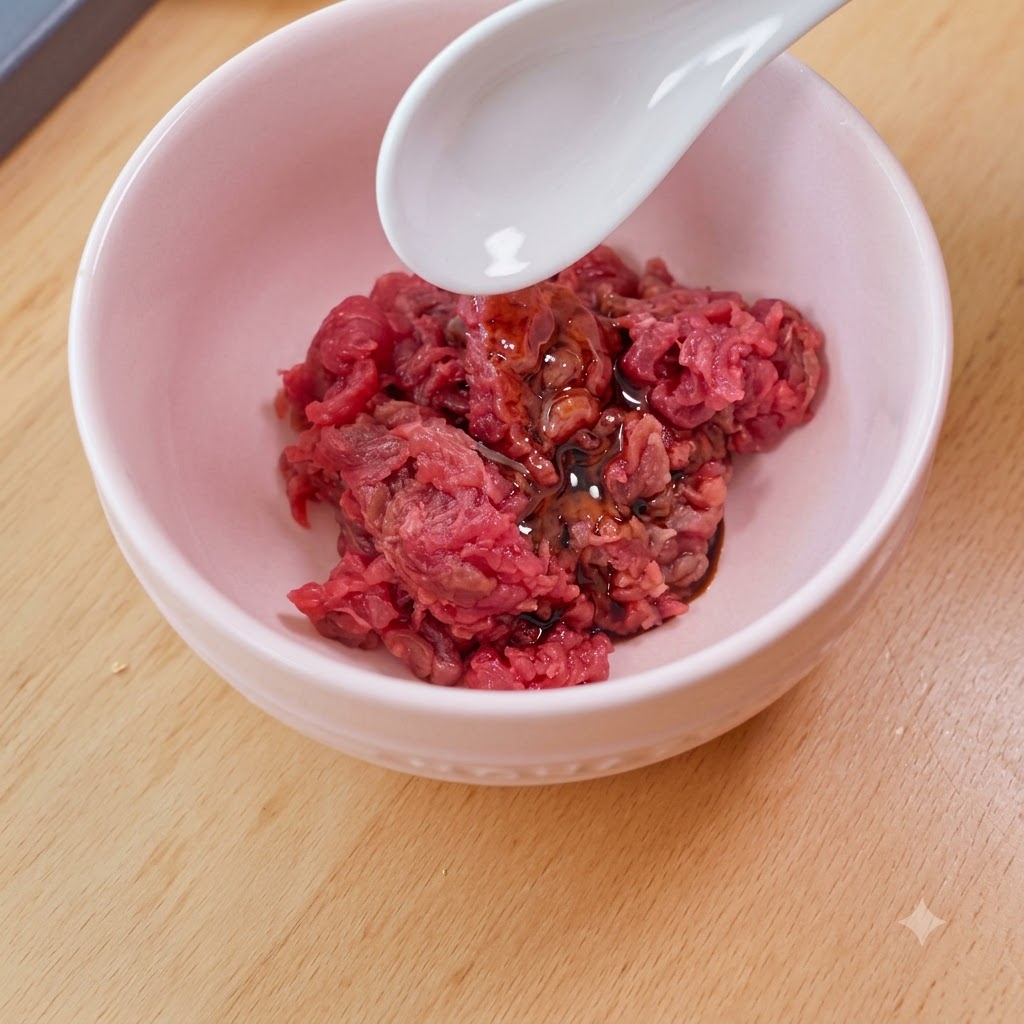 A white spoon adding starch to a pink bowl filled with diced raw beef, soy sauce, and oil.