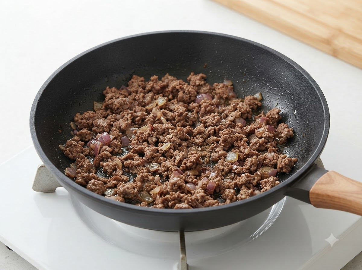 Cooked minced beef and onions mixed together inside a frying pan.