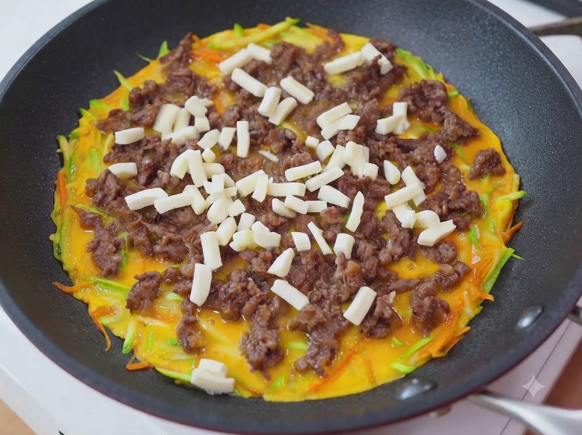 Shredded mozzarella cheese being sprinkled over the beef and egg layer in the pan.