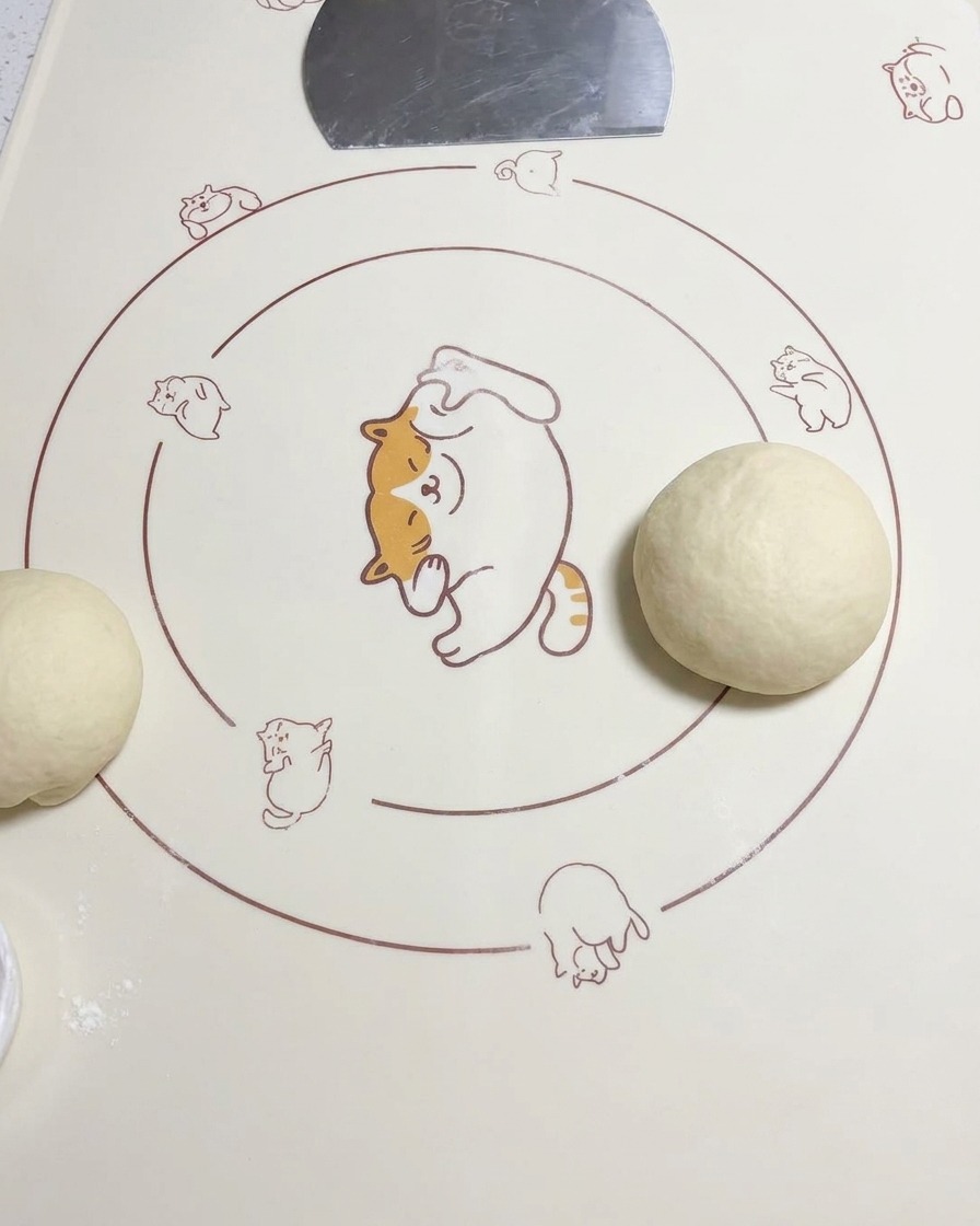 A rounded dough ball sitting on a silicone mat next to another piece of rolled dough.