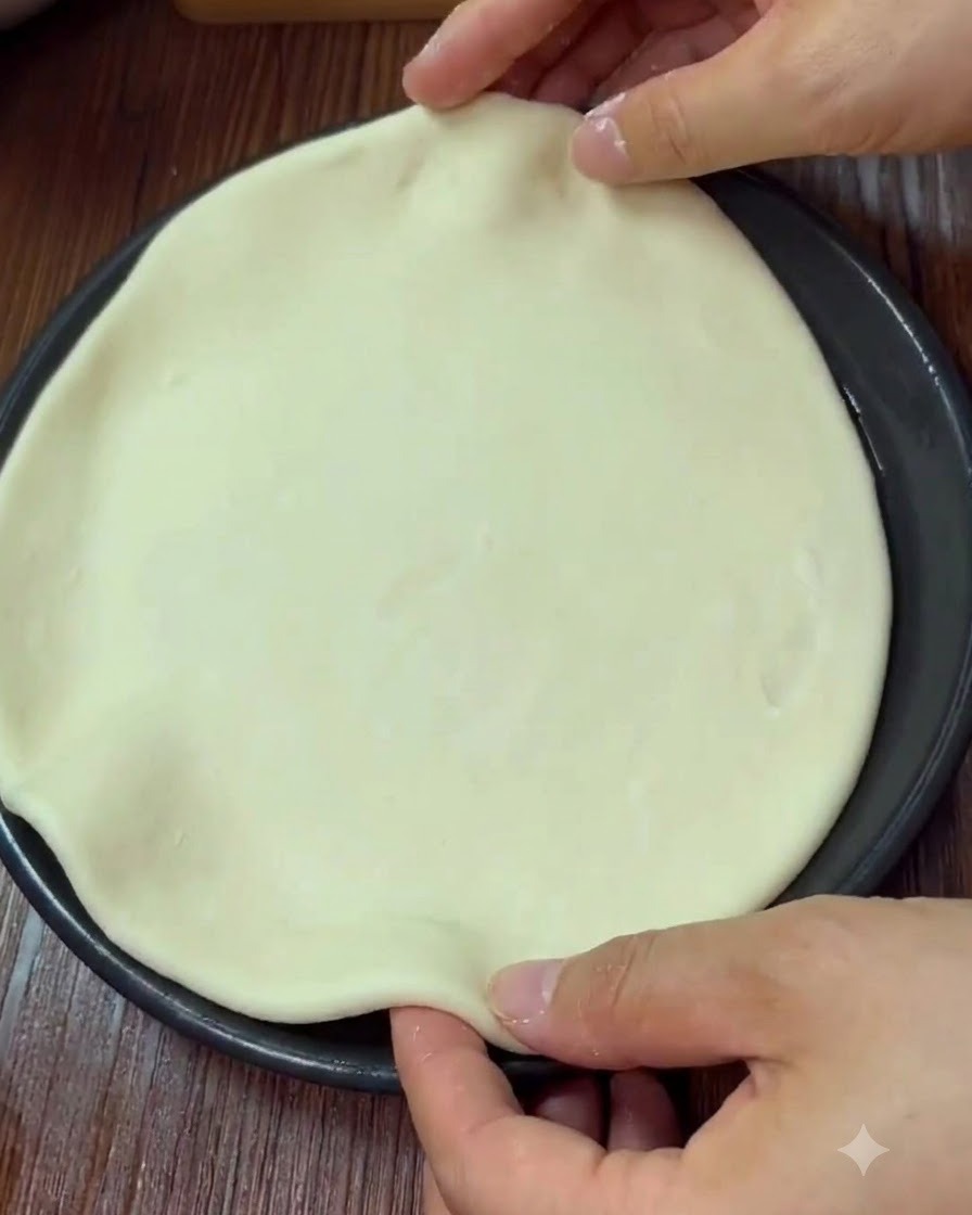Hands shaping and pinching the edge of a round pizza dough inside a baking pan.