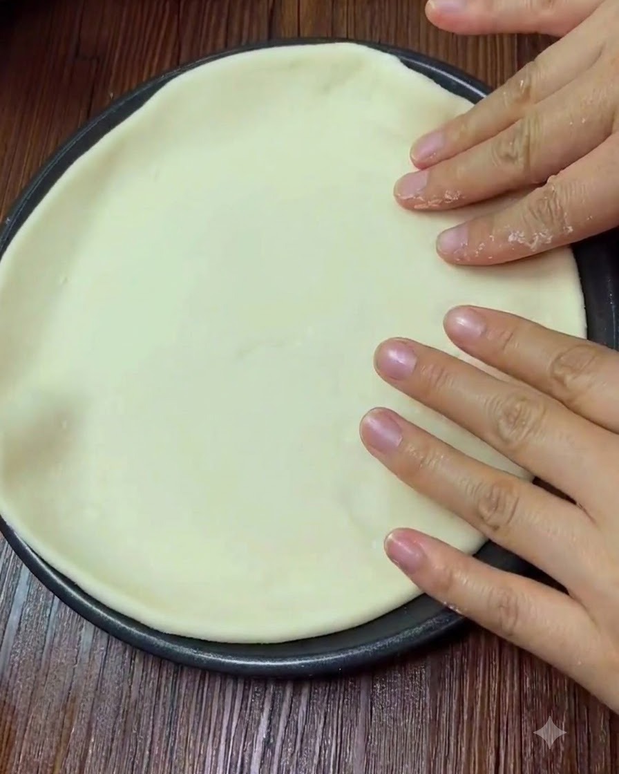 Hands pressing down gently on the surface of a flattened pizza dough.