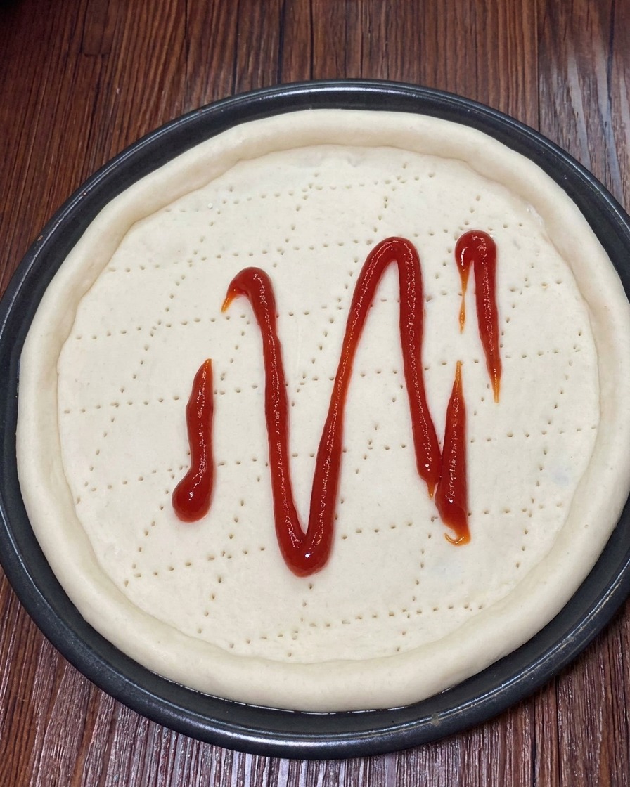Shredded mozzarella cheese being sprinkled evenly over the tomato sauce on the pizza dough.