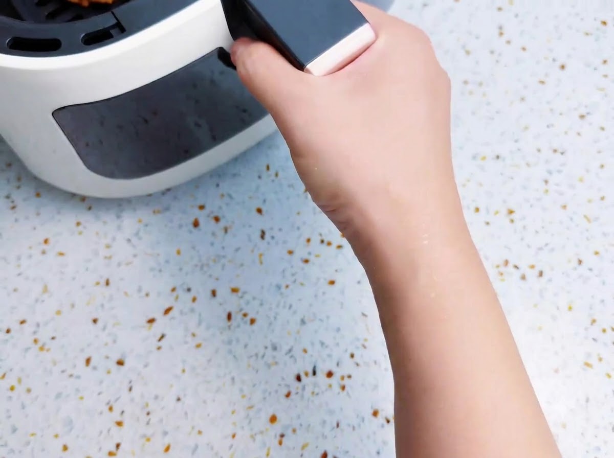 An air fryer basket loaded with bacon-wrapped potato sticks being pushed into the air fryer body.