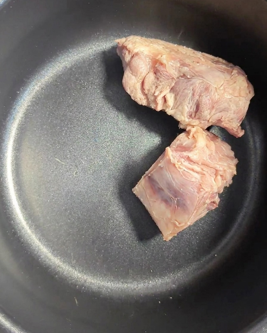 Rinsed pork bones sitting inside a dark rice cooker pot.