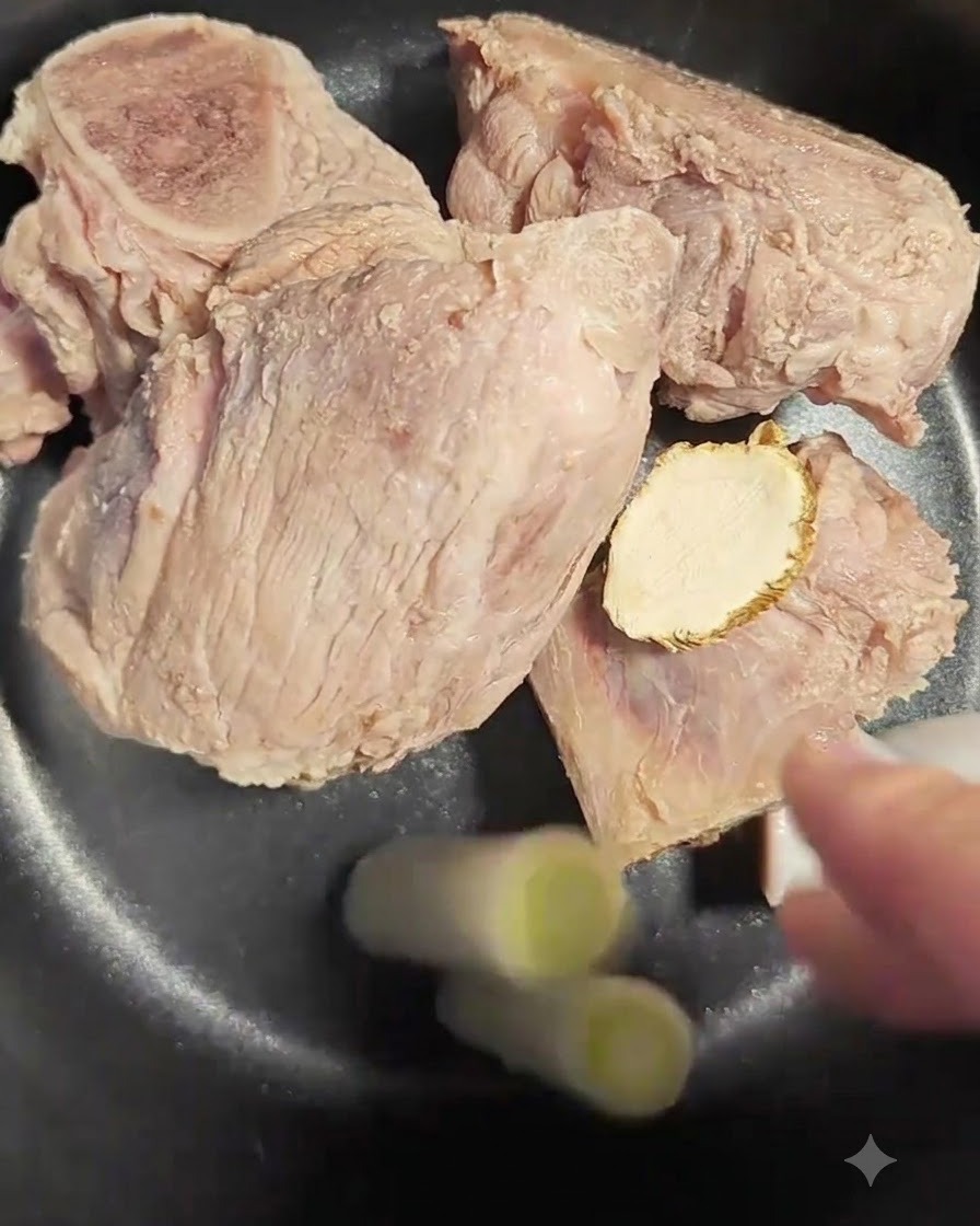 Two pieces of scallion white being added to the pot with bones and angelica root.