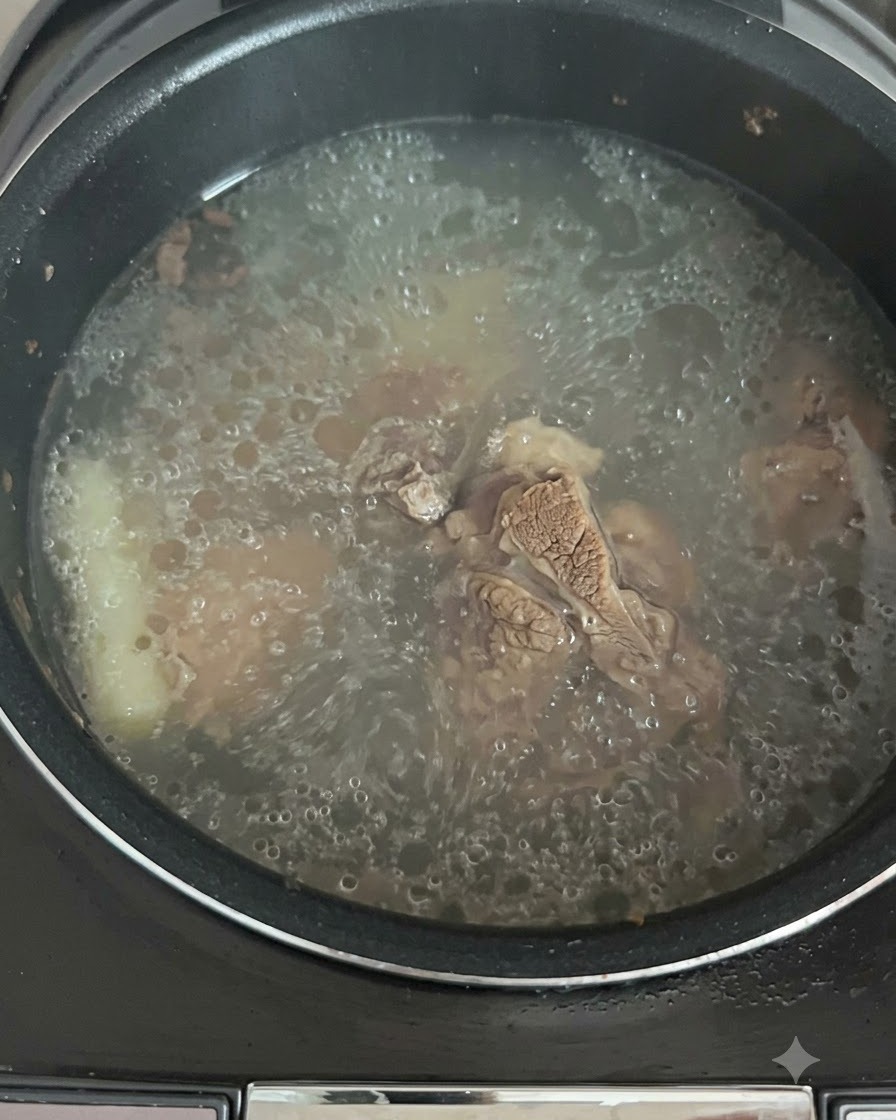 The broth actively bubbling and boiling inside the rice cooker pot.