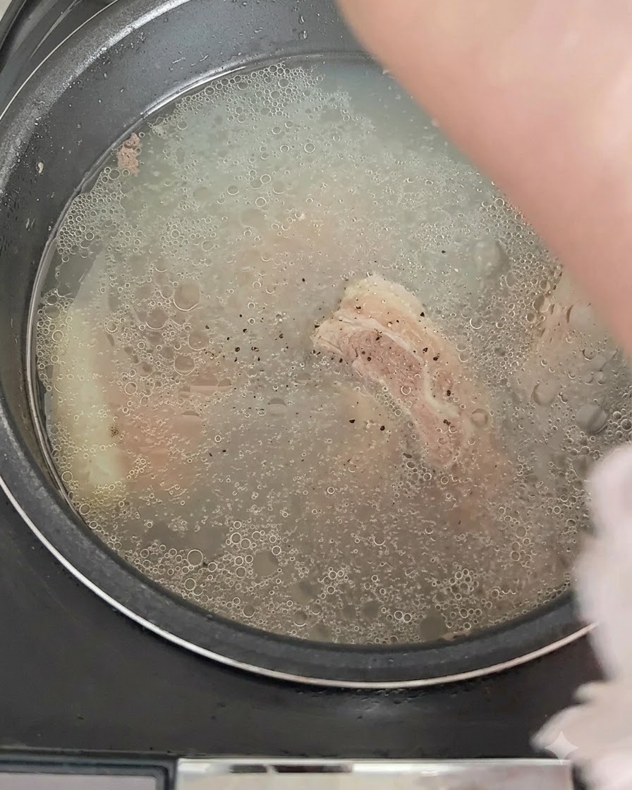 Black pepper being sprinkled over the bubbling broth in the rice cooker.