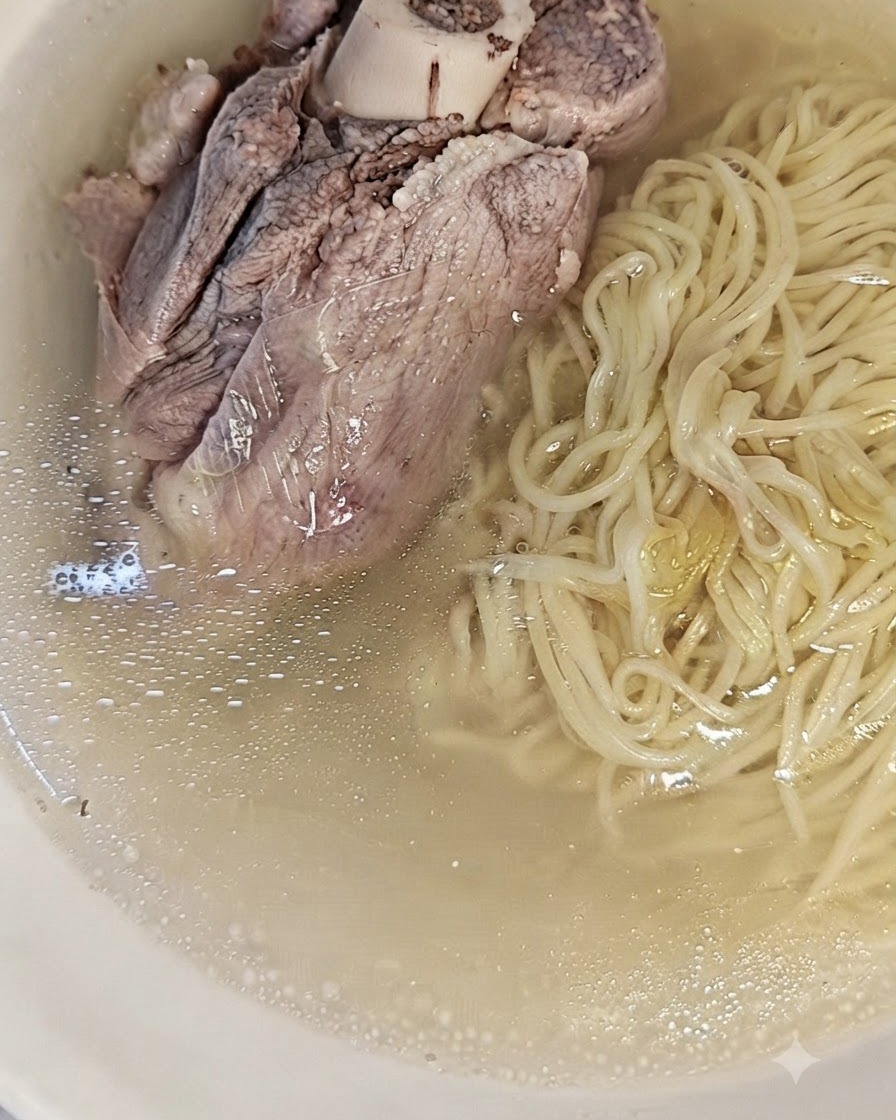 Cooked noodles resting in a bowl alongside the clear, strained pork broth.