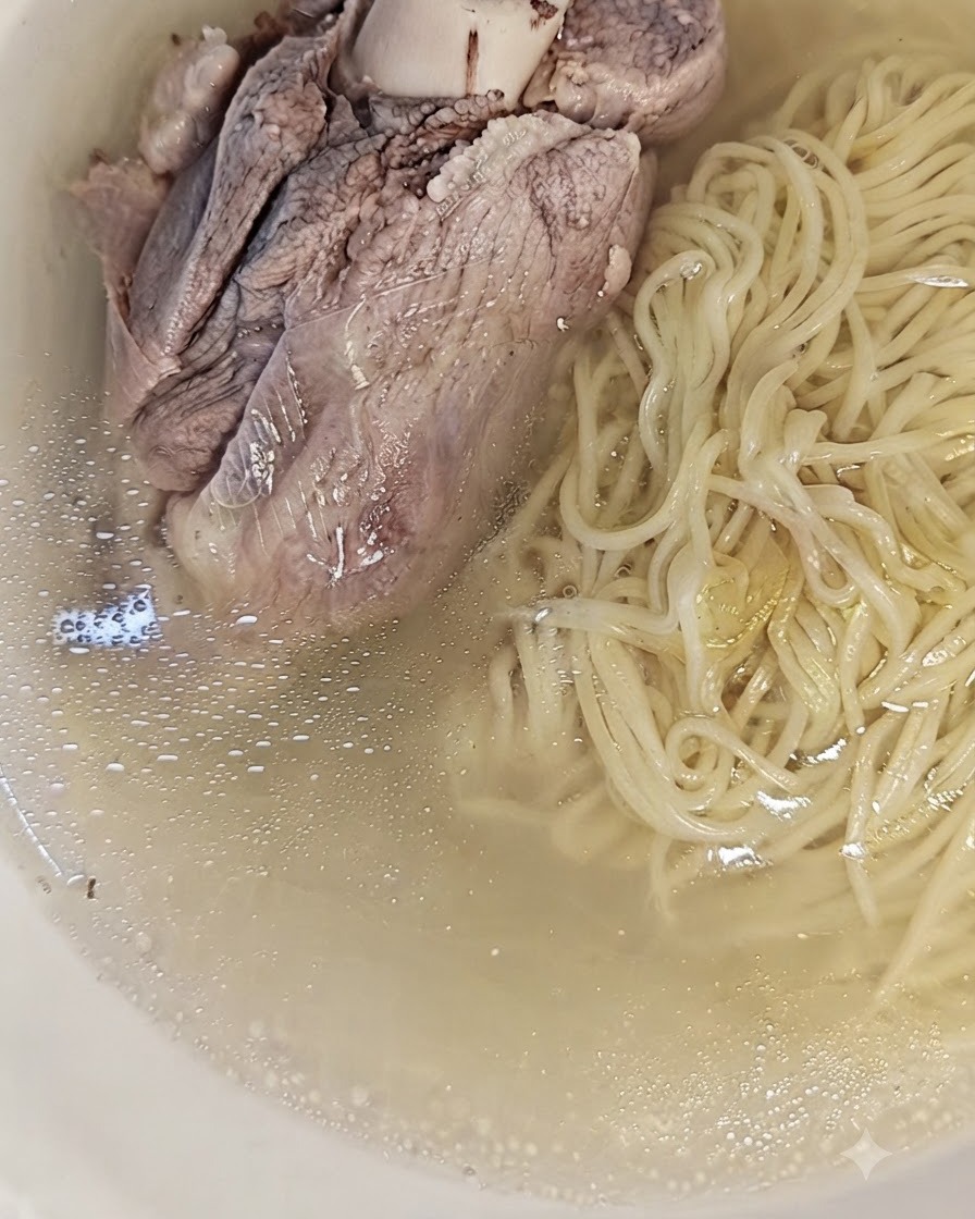 A large cooked pork bone placed on top of the noodles and broth in a bowl, ready to serve.