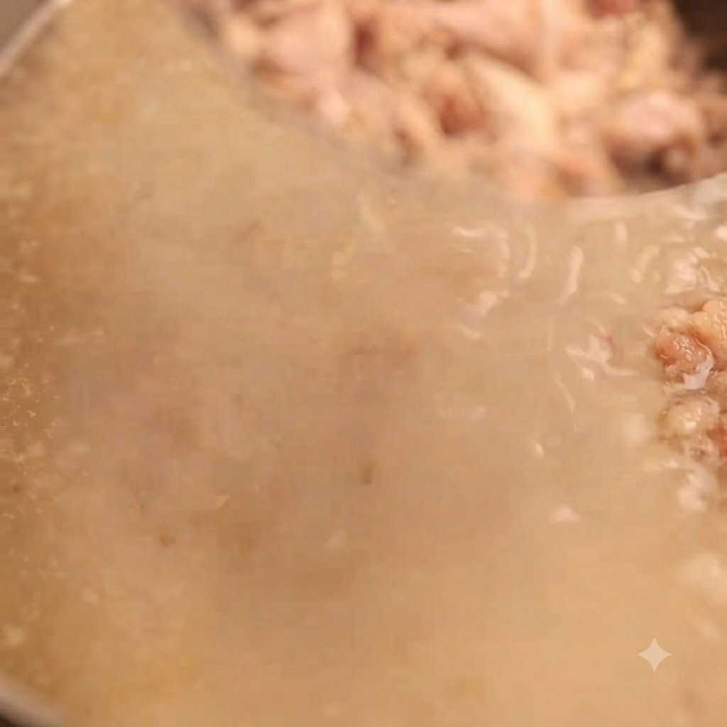 Rich, milky white pork bone broth being strained through a fine-mesh sieve to catch remaining meat bits.