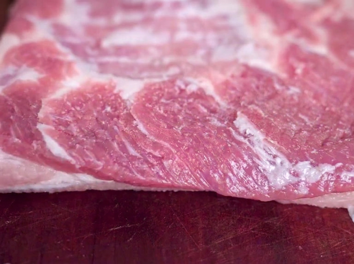 Close-up of a raw slab of pork belly resting on a wooden cutting board with visible salt grains.