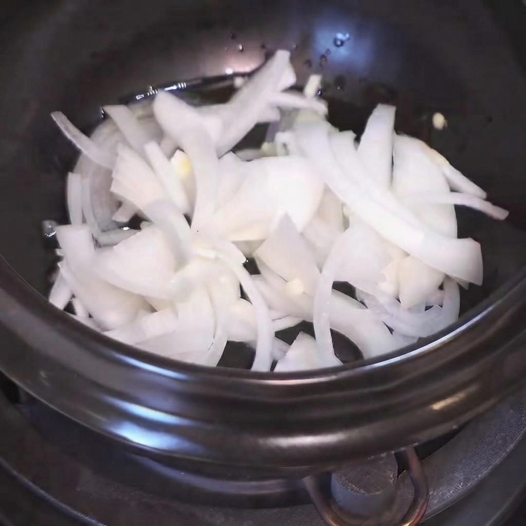 Sliced white onions sizzling in oil inside a dark pot.
