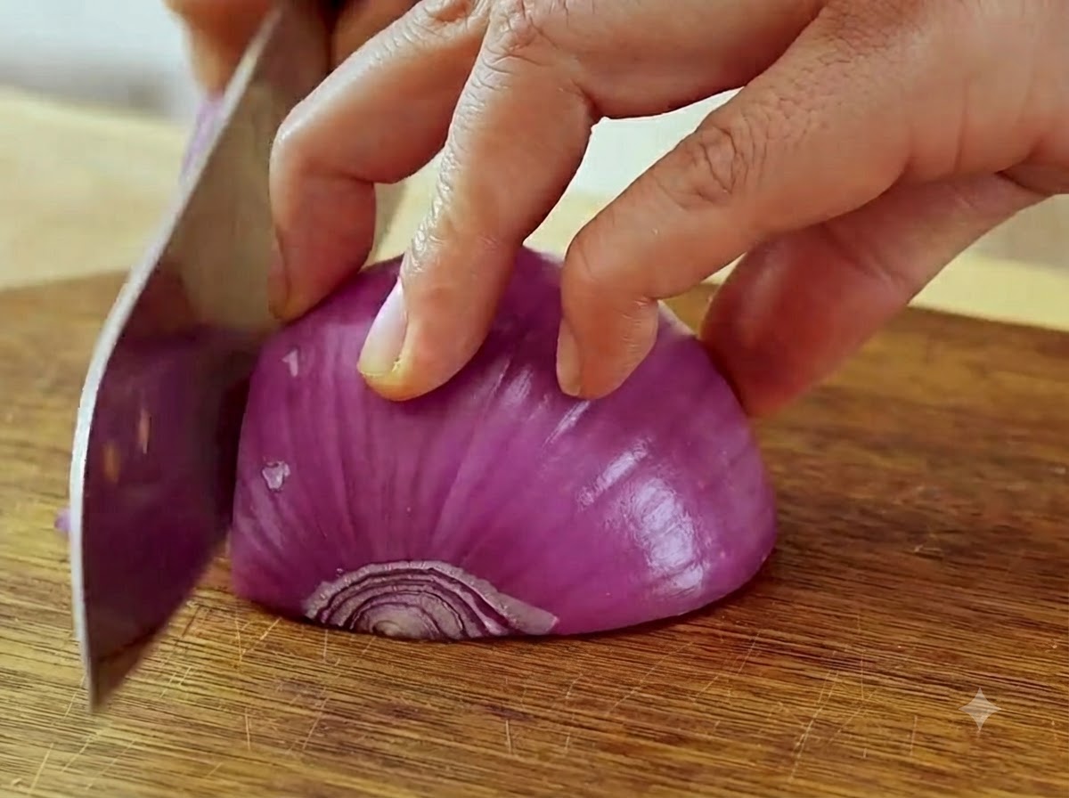Hands holding a knife and slicing a red onion into thin strips on a cutting board.