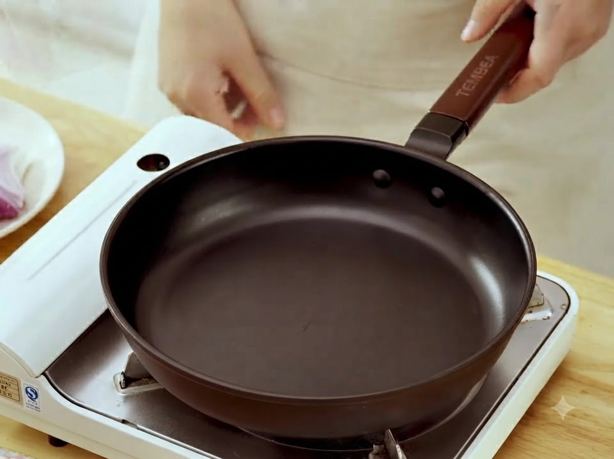 A black frying pan sitting on a portable stove with a hand holding the handle.