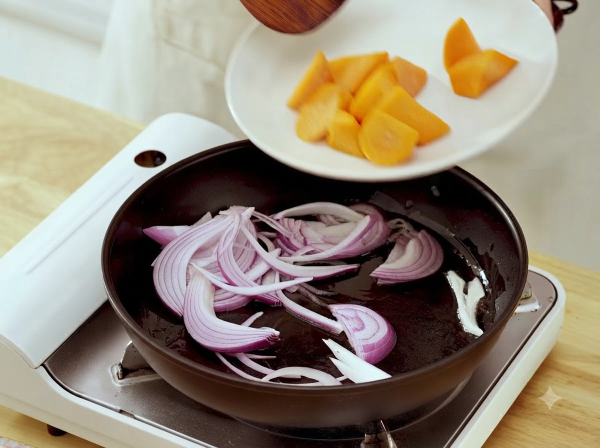 Carrot chunks being transferred from a white plate into a frying pan containing sautéed onion strips.